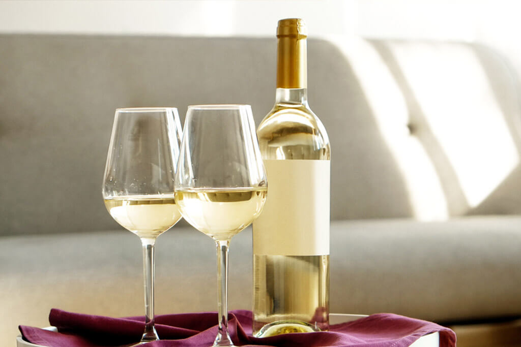 Garrafa de vinho branco ao lado de duas taças, sobre mesa.